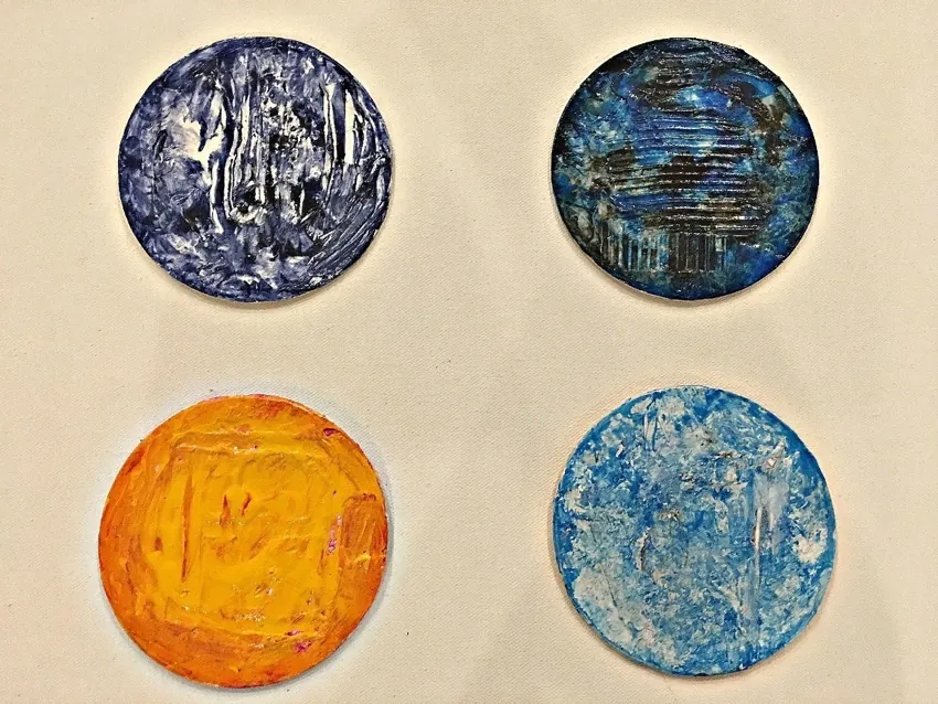 Four textured, circular paintings by Clara Berta are arranged in a grid on a light background. Featured at the Art Show, the works include deep blues, orange-yellow, and light blue with white streaks—each piece rich in color and texture.