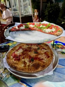 An airy, golden-crust square pizza topped with vibrant red sauce and creamy burrata cheese, elegantly served on a silver platter amidst the lemon trees at Truly Pizza.