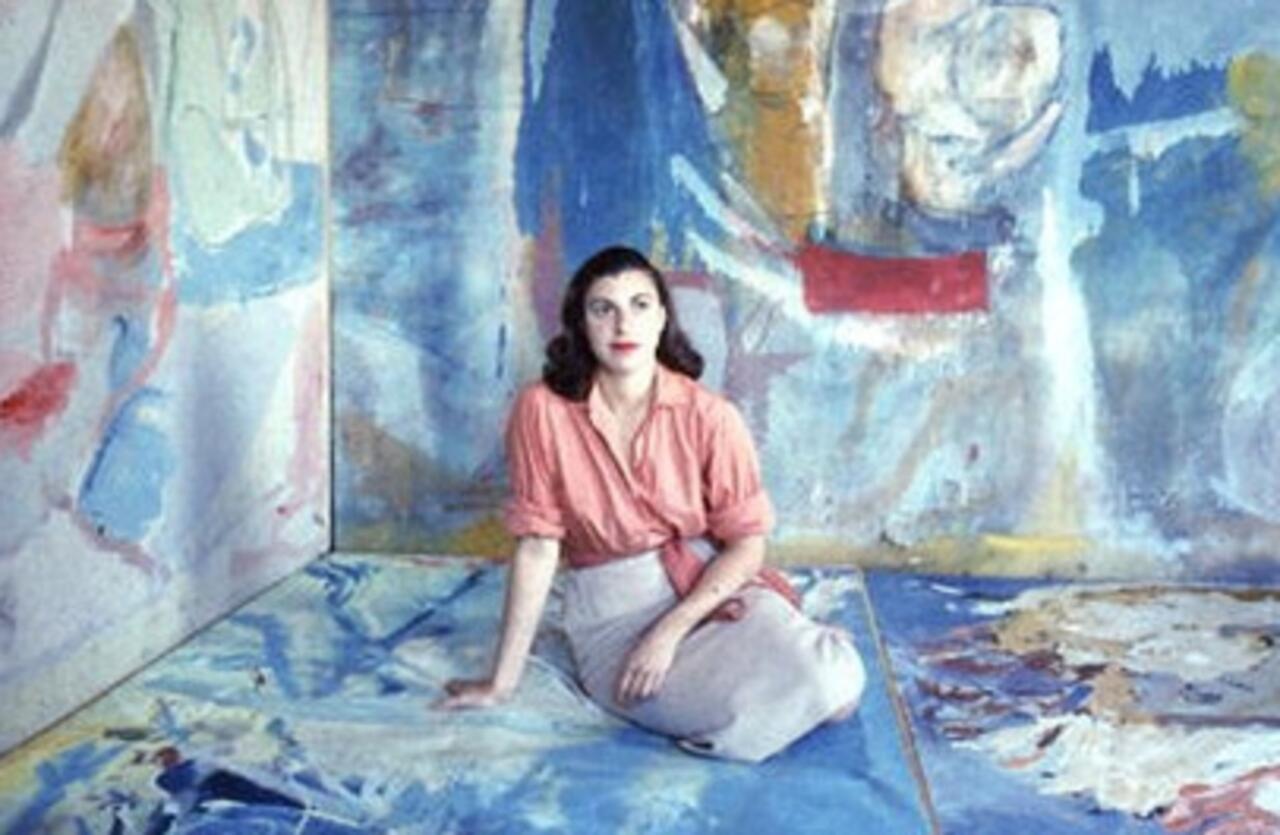 Renowned abstract expressionist artist Helen Frankenthaler posing in her studio, surrounded by her large-scale color field paintings laid out on the floor.