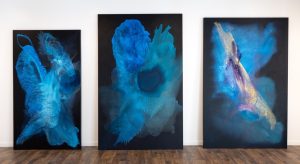 Clara Berta large-scale abstract blue triptych with three fluid panels on a dark background.