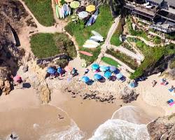 Aerial drone view of Shaws Cove in Laguna Beach, showing the crescent-shaped sandy shoreline, turquoise ocean water, and coastal homes sitting on the rocky bluffs above.