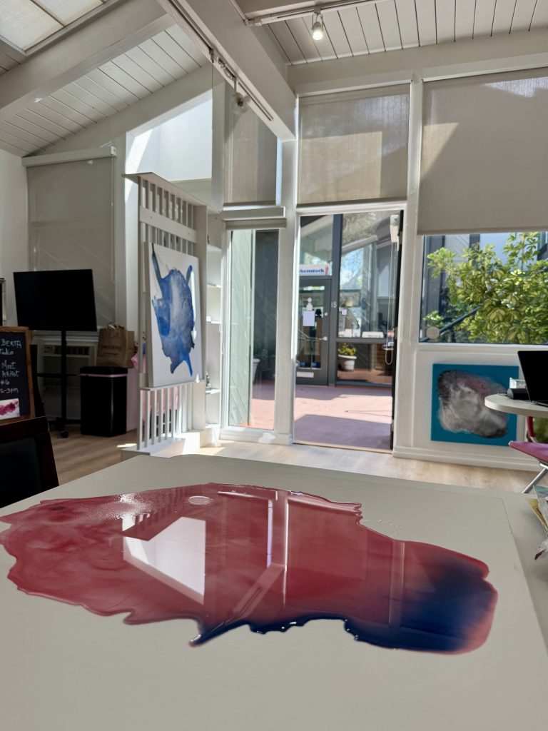 Clara Berta’s Laguna Beach studio bathed in natural light, featuring an abstract canvas on the table and a serene view of the outdoors.