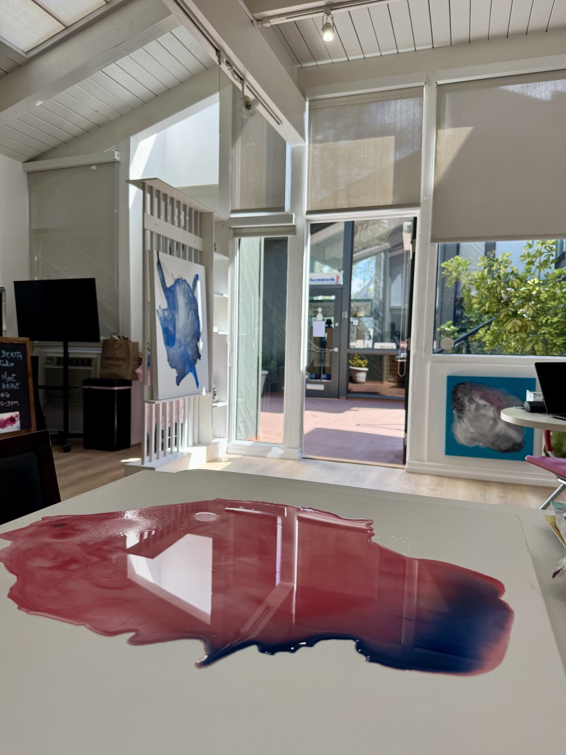 Clara Berta's Laguna Beach studio bathed in natural light, featuring an abstract canvas on the table and a serene view of the outdoors.