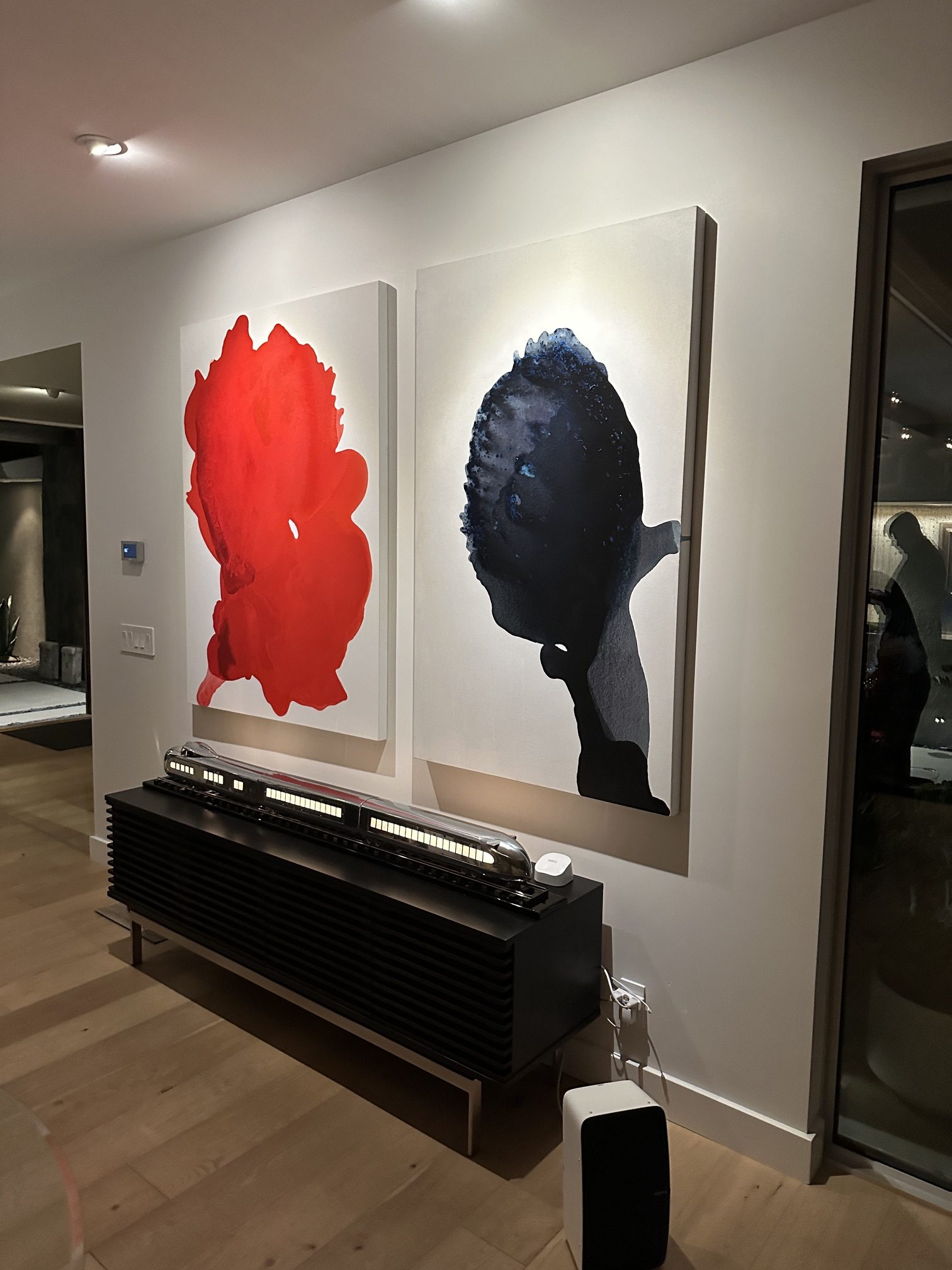 Large-scale abstract acrylic paintings by Clara Berta displayed together in a modern collector's living room. A vibrant, textured red painting with organic forms hangs beside a deep, calm blue abstract piece, showcasing a balanced color study of intense vitality and serene depth.