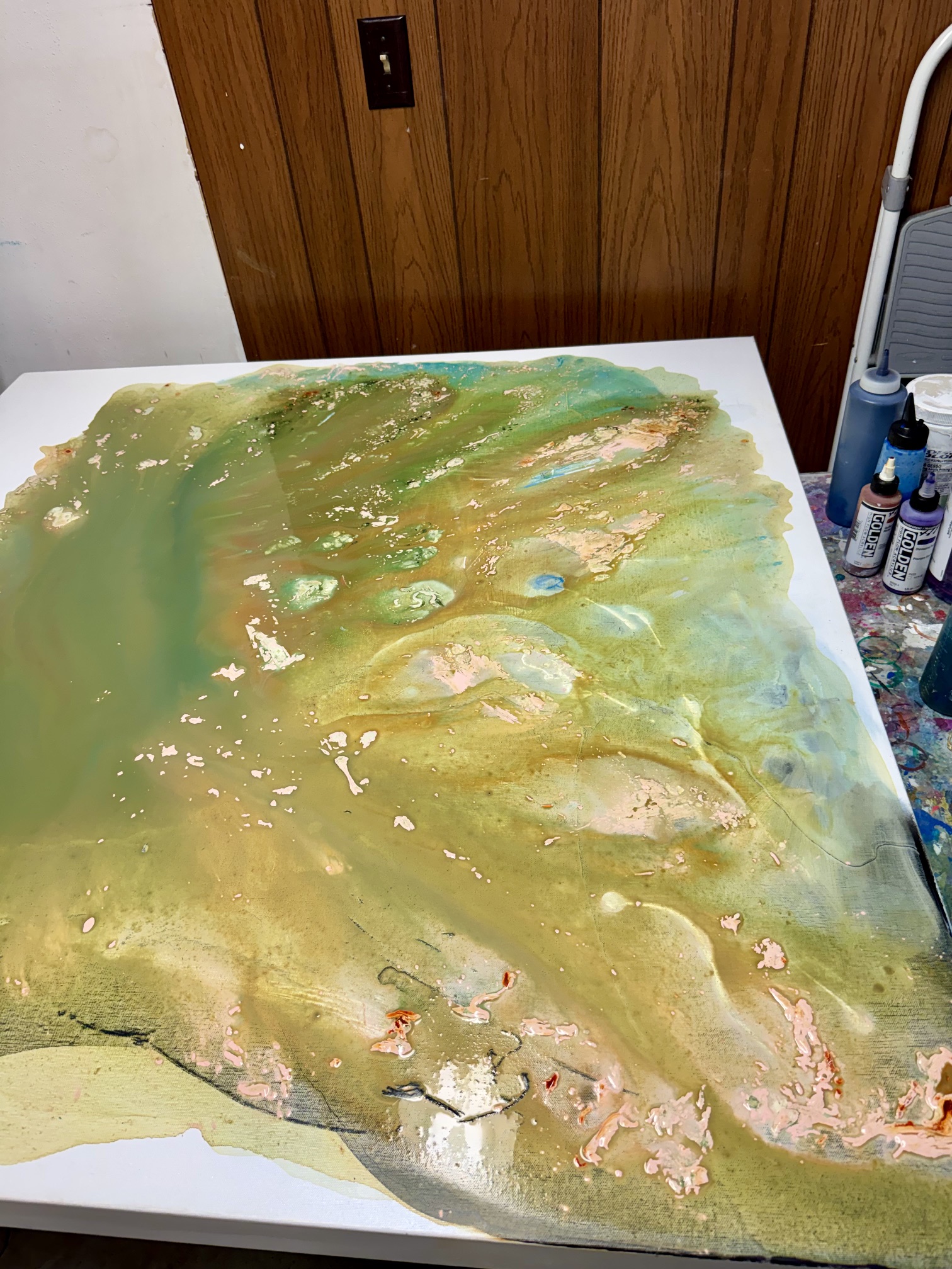Wet fluid art painting with sandy earth tones, vibrant green, and hot pink sitting flat on a studio table, capturing the moment of finding my creative flow.
