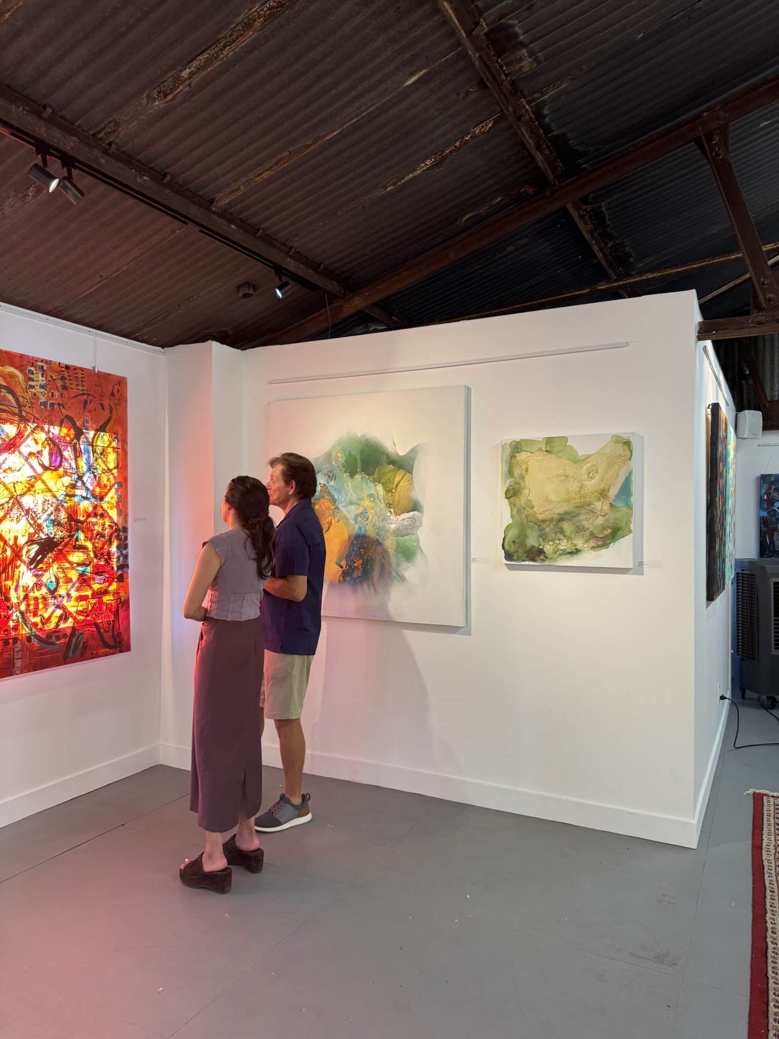 Collectors viewing green and gold abstract paintings Foggy Scape and Serenity by Clara Berta.