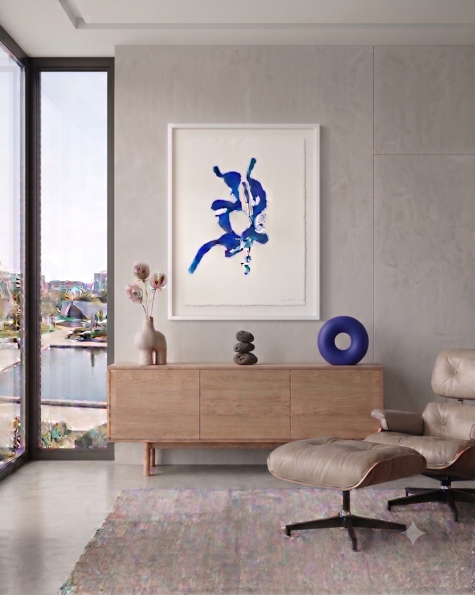 Framed blue abstract painting by Clara Berta above a wood credenza styled with small volcanic stones and a blue torus sculpture.